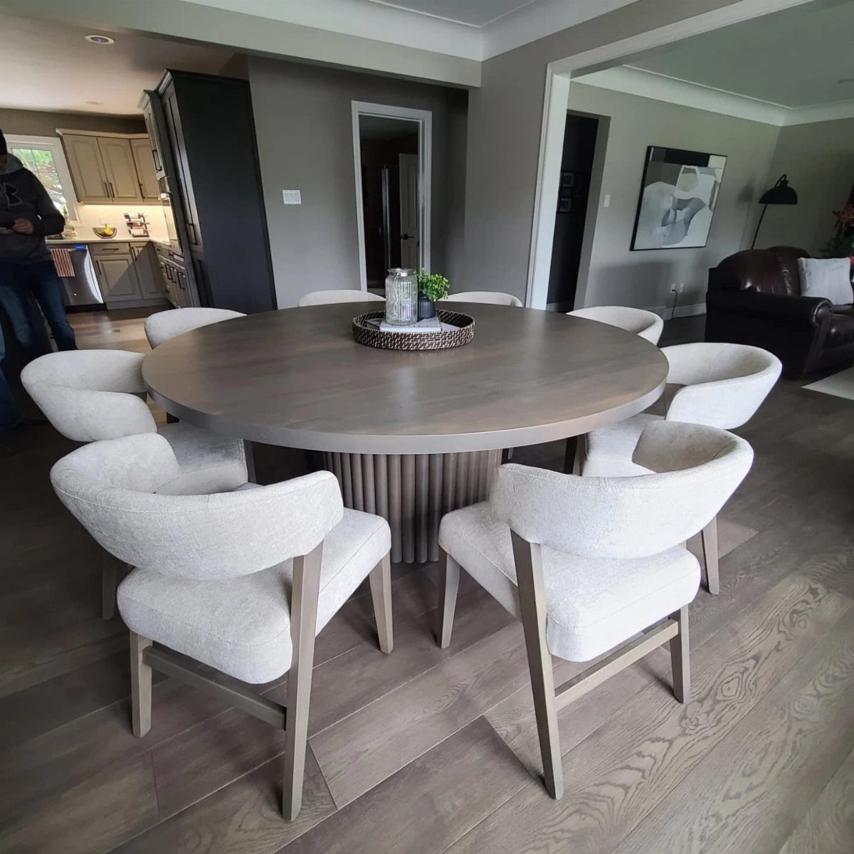 Round grey wooden dining table with white upholstered chairs in a modern room