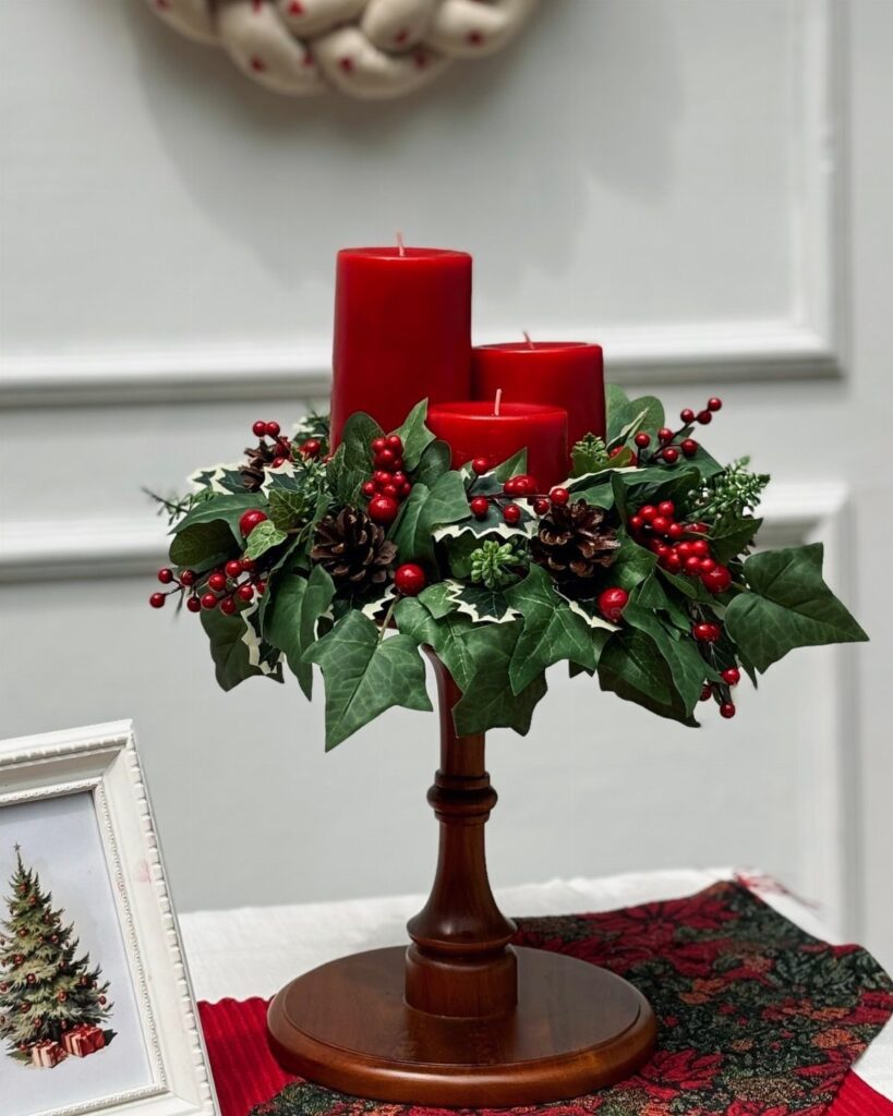 Red pillar candles in a wooden holder with ivy, berries, and pinecones.