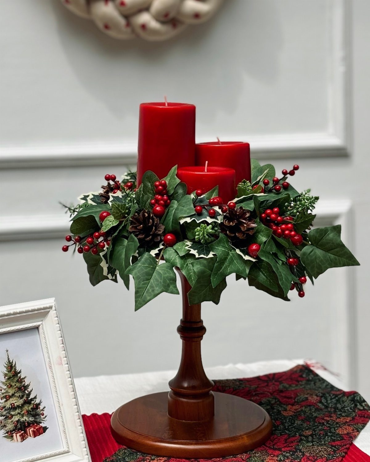 Red pillar candles in a wooden holder with ivy, berries, and pinecones.