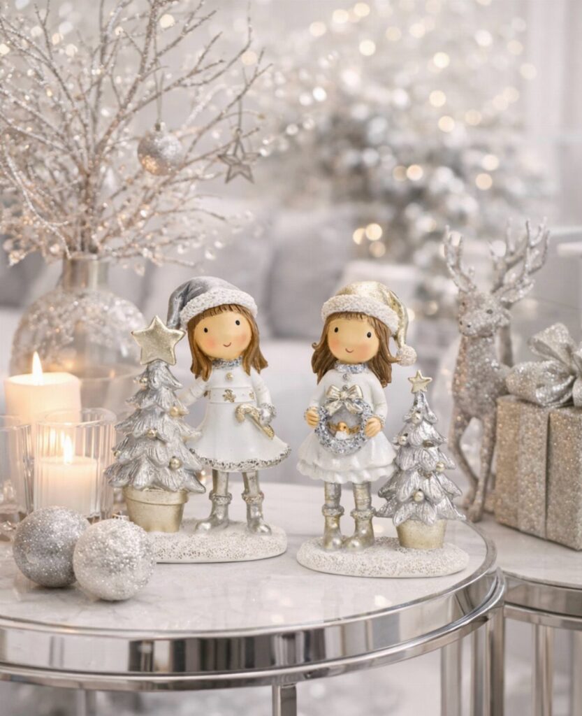 Winter figurines and silver glitter decorations on a white marble table with candles.