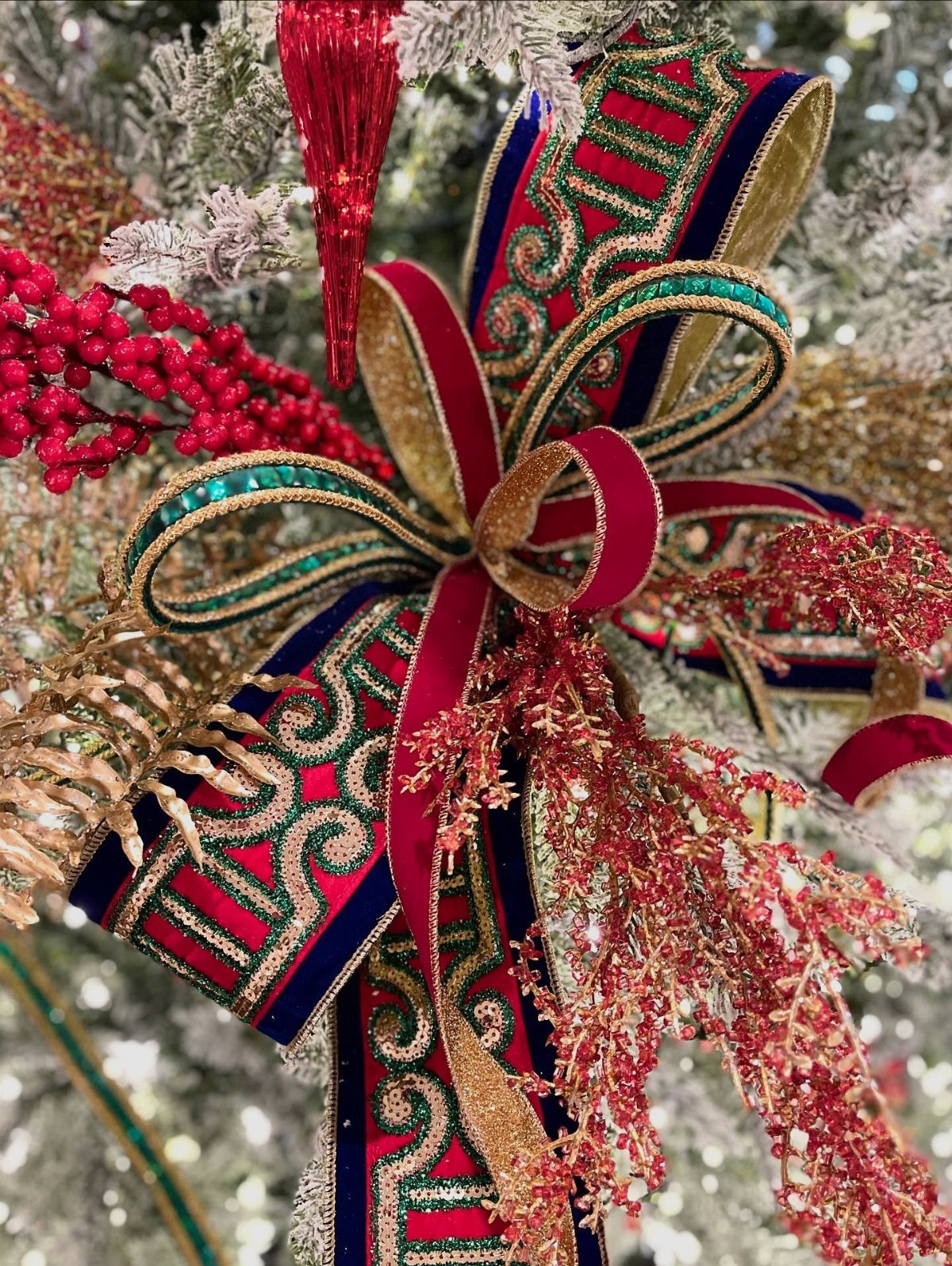 Red, gold, and green ornate ribbons tied in a bow on a Christmas tree.