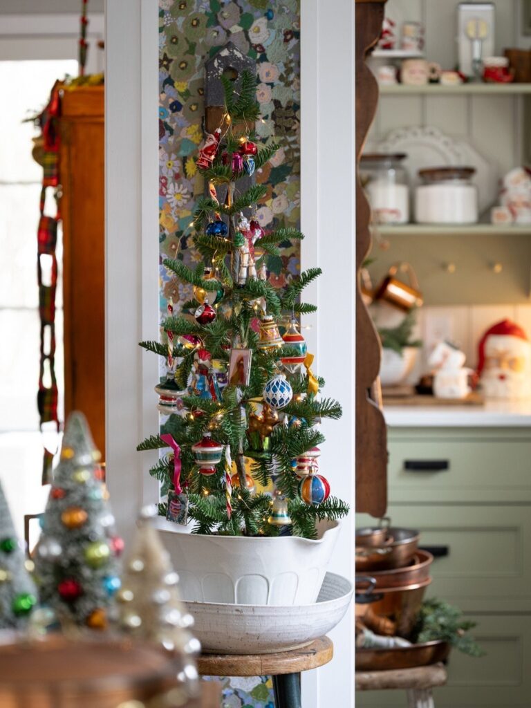Small decorated Christmas tree in a white pot on a wooden kitchen stool.