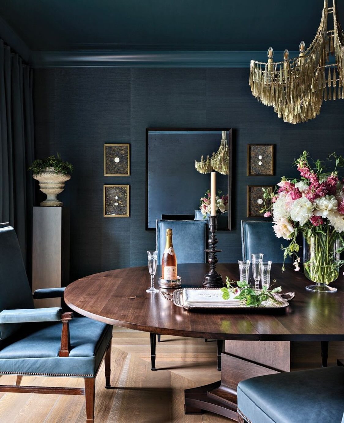 Dark blue dining room with a wooden oval table and gold chandelier.