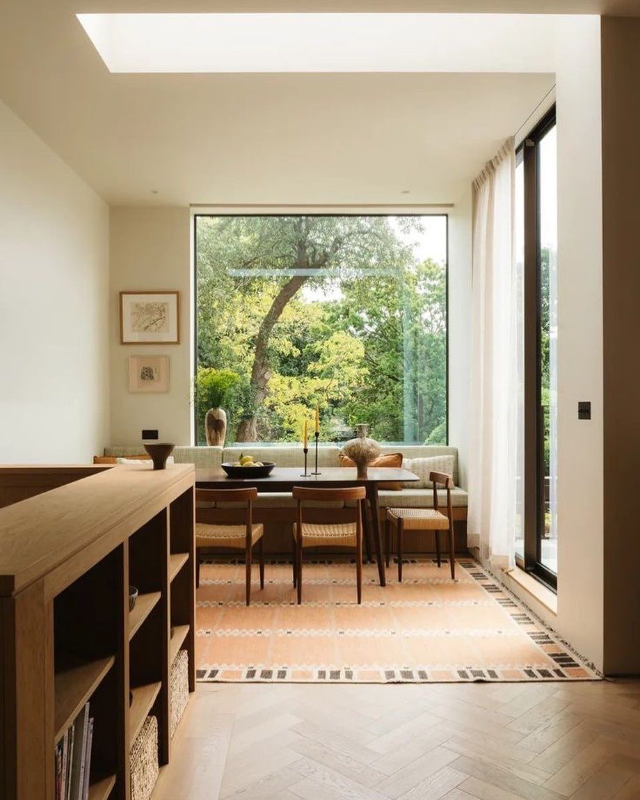 Dining table and built-in bench positioned in front of a large window with greenery.