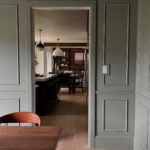 Sage green wall paneling with a chair rail leading into a modern kitchen.
