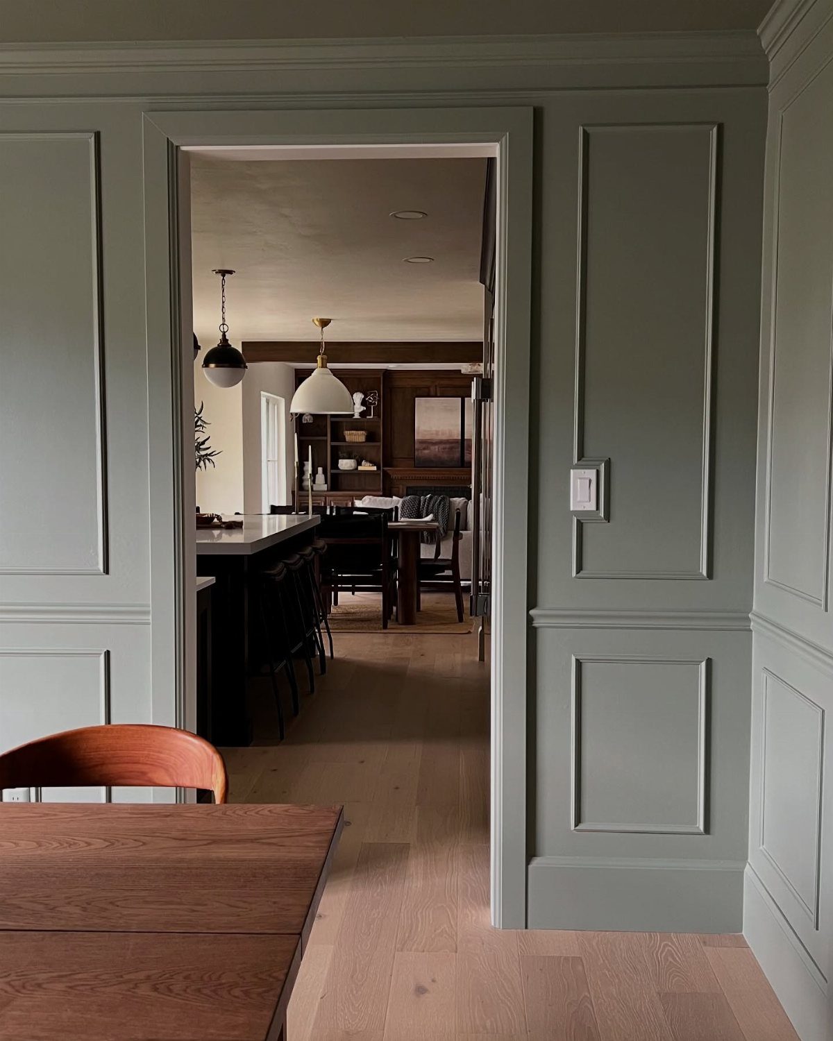 Sage green wall paneling with a chair rail leading into a modern kitchen.