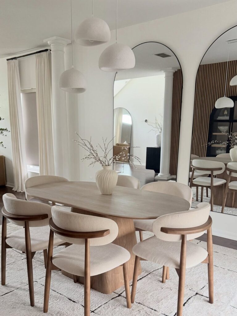 Modern dining room with oval wooden table, cream curved chairs, and white pendant lights.
