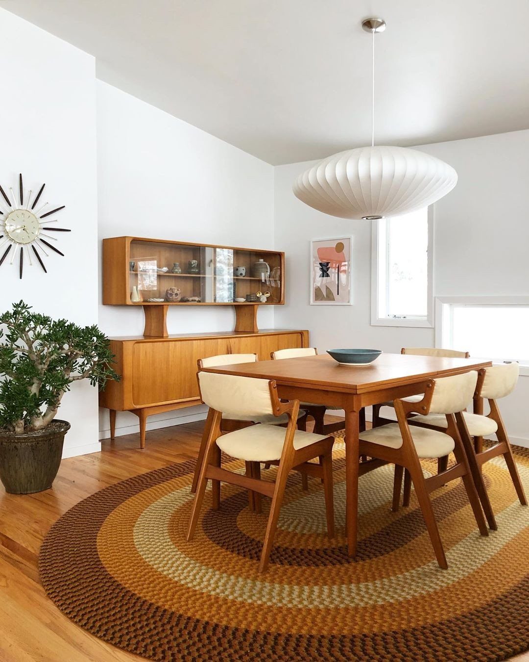 Mid-century modern dining room with wooden furniture, white pendant light, and circular rug.
