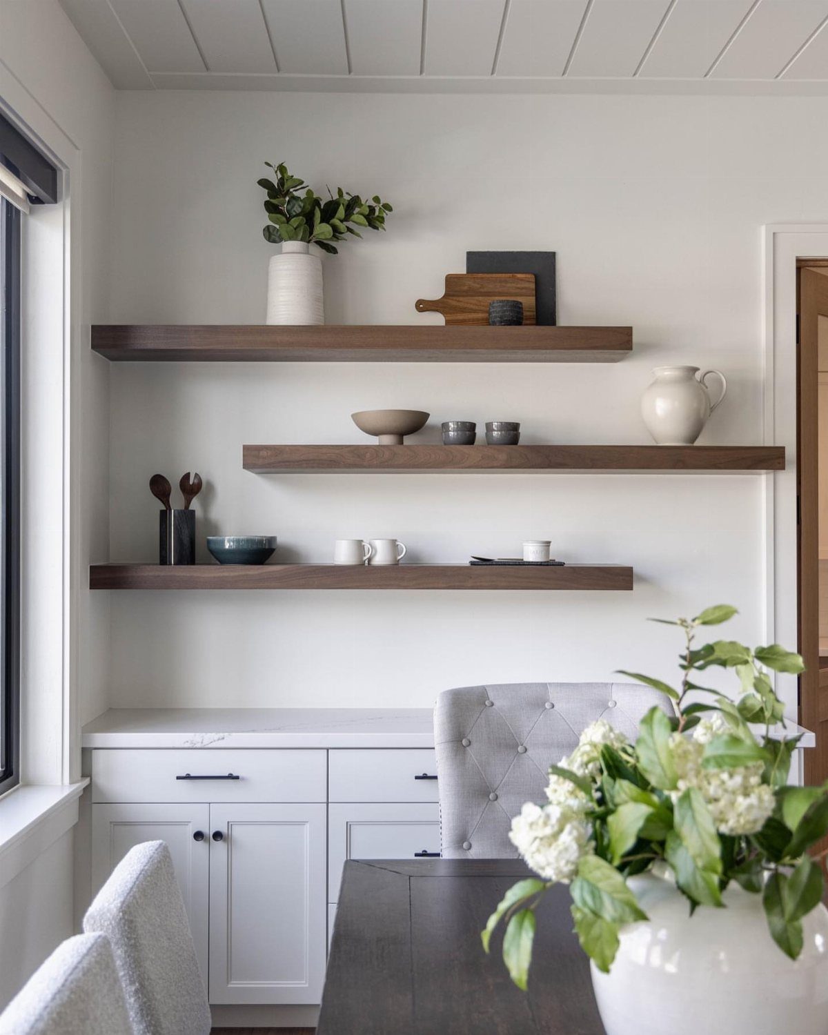 Dark wood floating shelves above a white sideboard with minimalist kitchen decor.