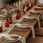 Wooden dining table with macrame runner, amber flower vases, and woven placemats.