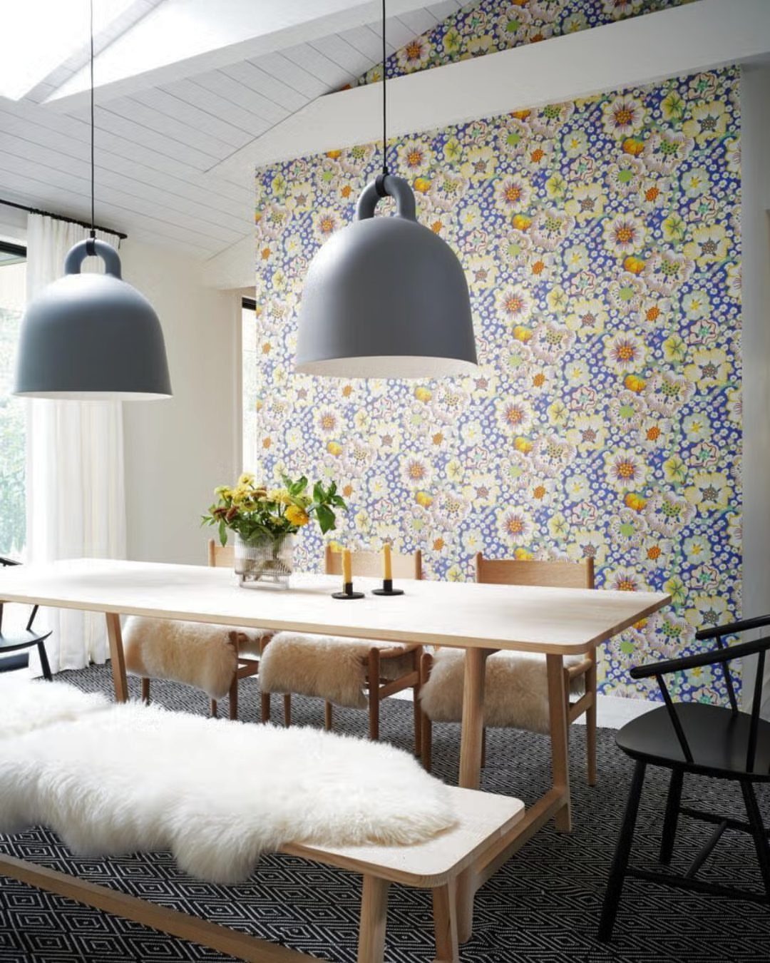 Light wood dining table with mismatched black and sheepskin chairs and a bench.