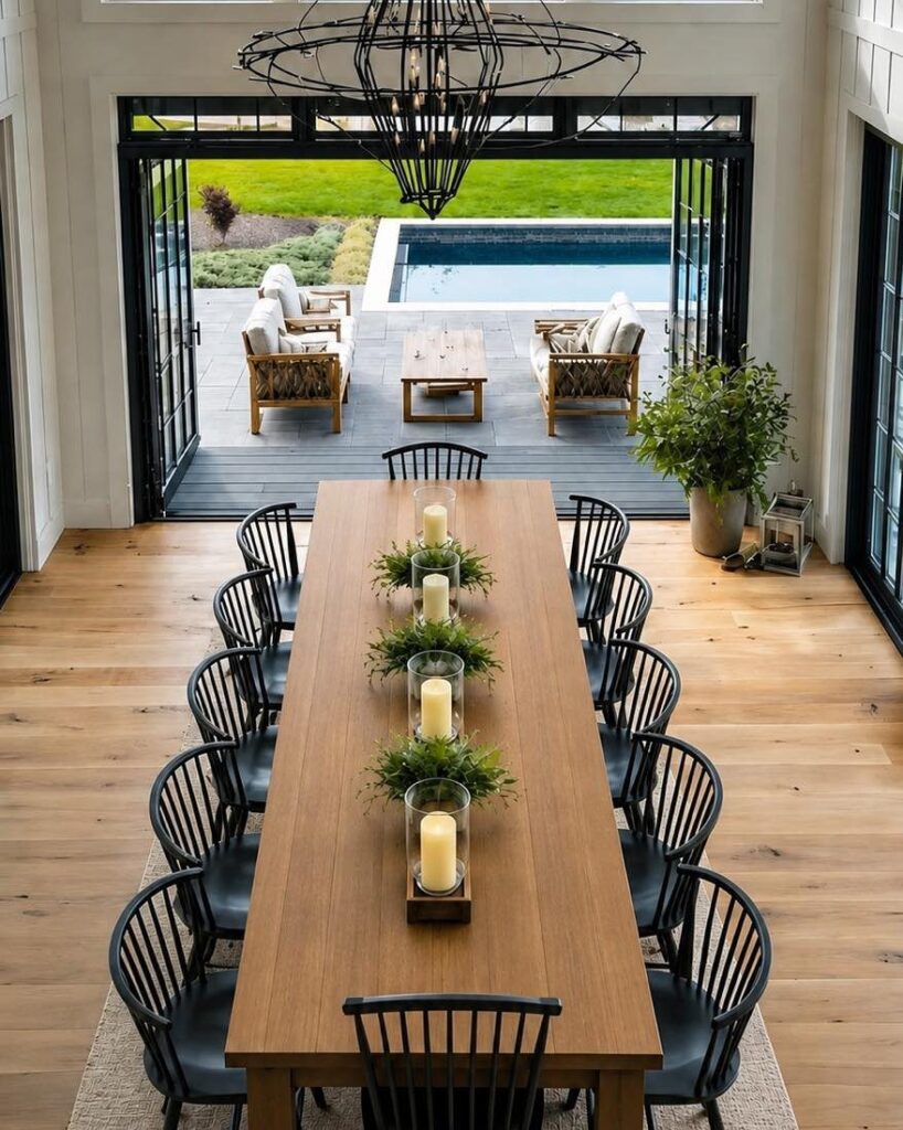 Long wooden dining table with twelve black chairs in a bright, open room.