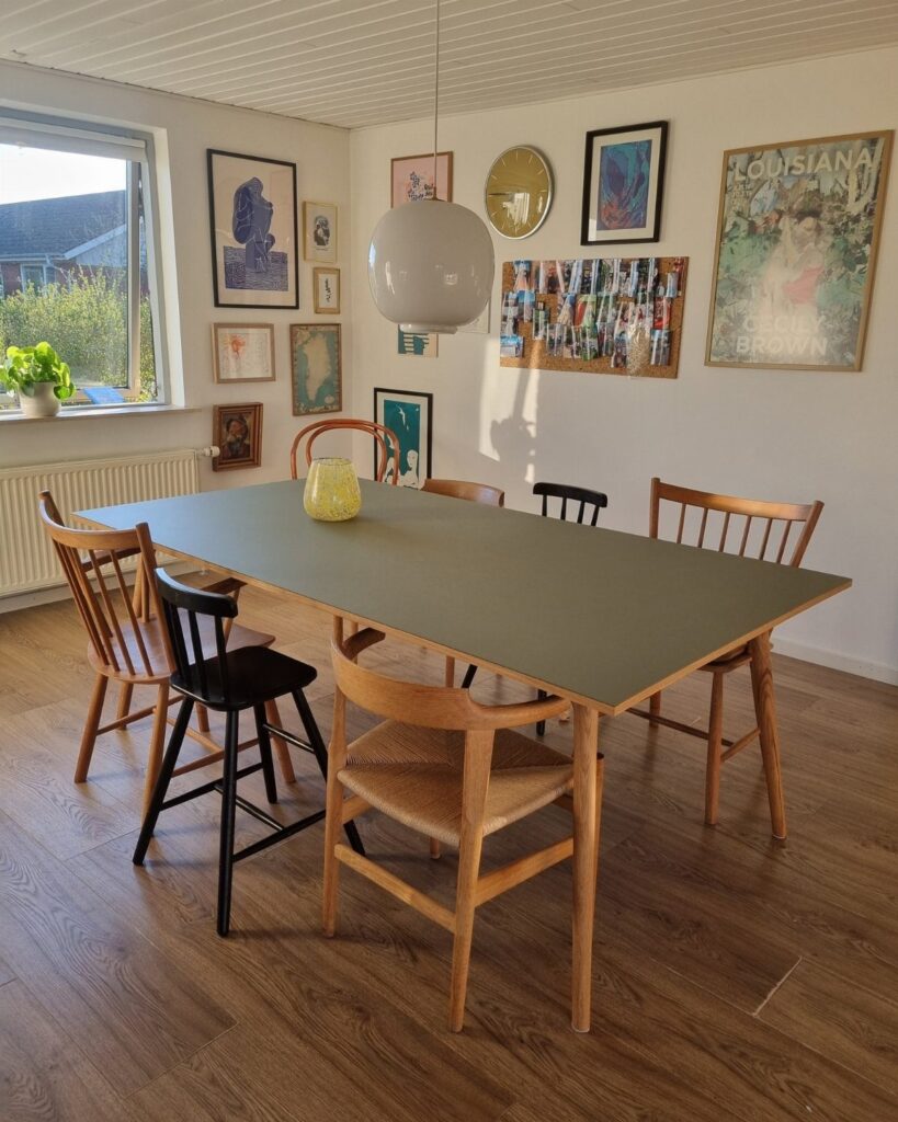 Grey dining table surrounded by mismatched wooden and black chairs in a bright room.
