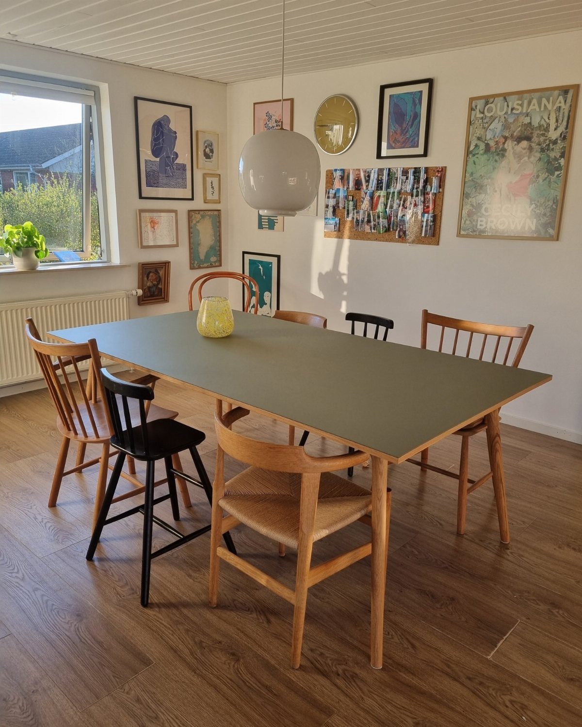 Grey dining table surrounded by mismatched wooden and black chairs in a bright room.