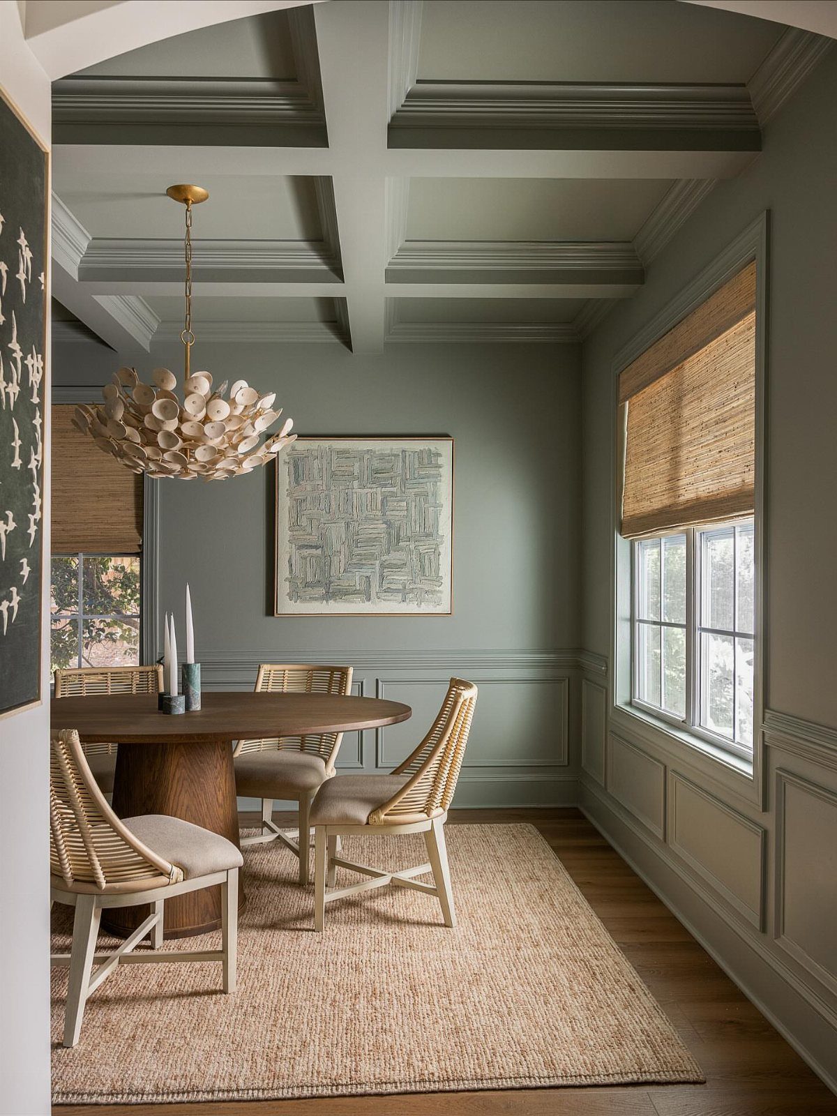 Dining room with evergreen fog green walls, wooden table, and woven chairs.