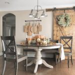 Dining room table with fall pumpkins and a leafy wreath on a barn door.