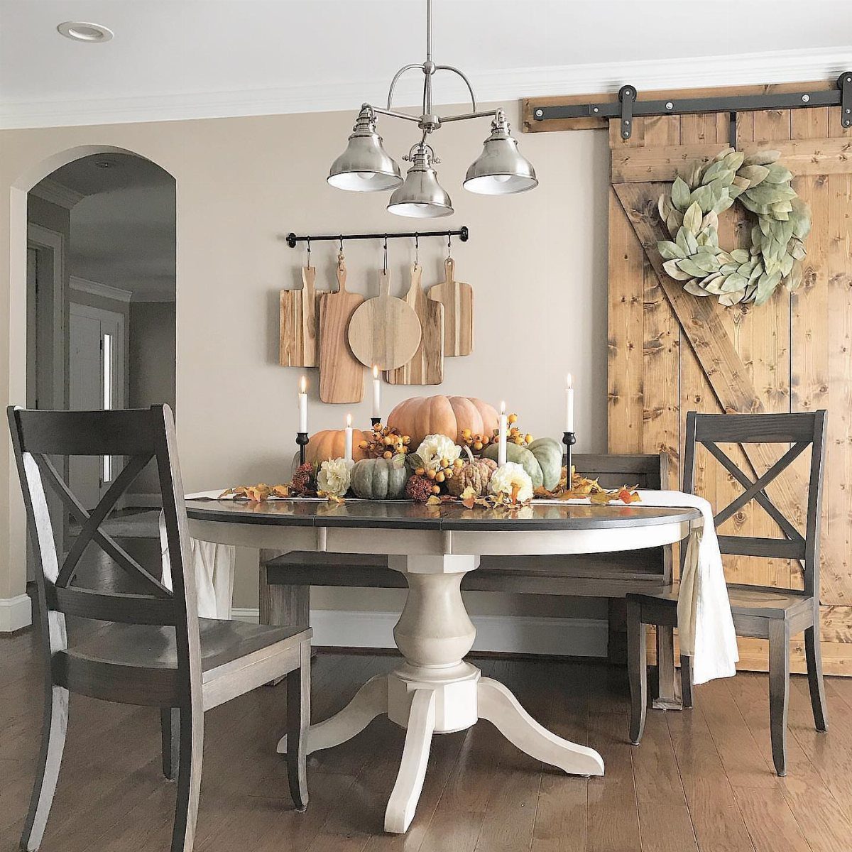 Dining room table with fall pumpkins and a leafy wreath on a barn door.