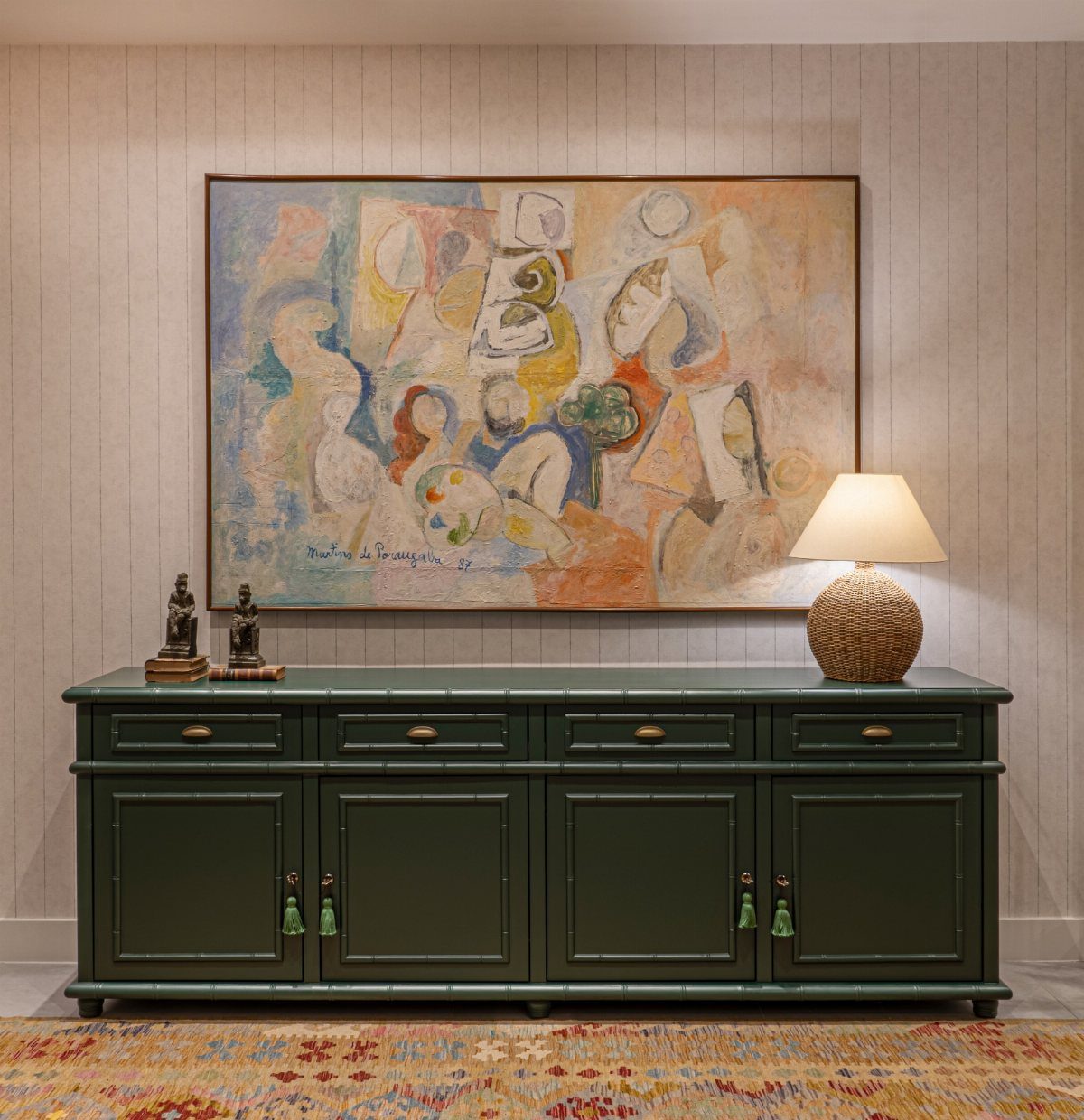 Dark green sideboard with a large abstract painting and lamp against a paneled wall.