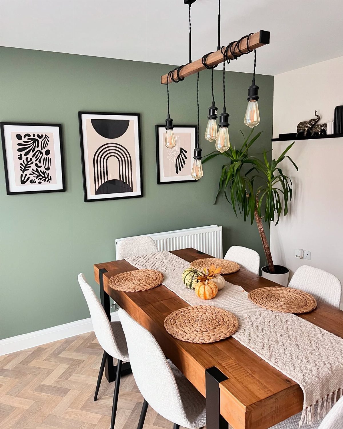 Dining room with sage green walls, wooden table, and modern abstract wall art.