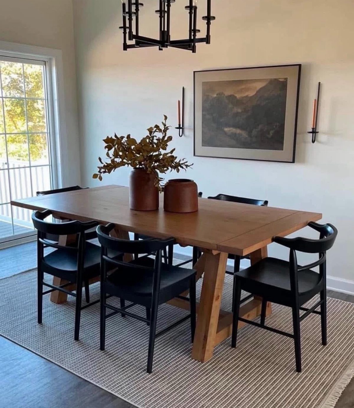 Wooden dining table and black chairs on a grey rug in a bright room.