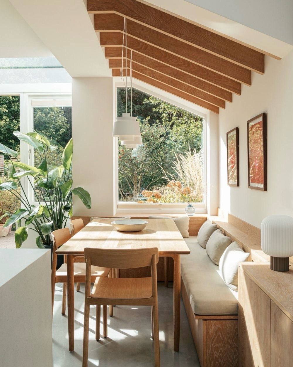 Light wood dining table with matching chairs and a cushioned wooden banquette seat.
