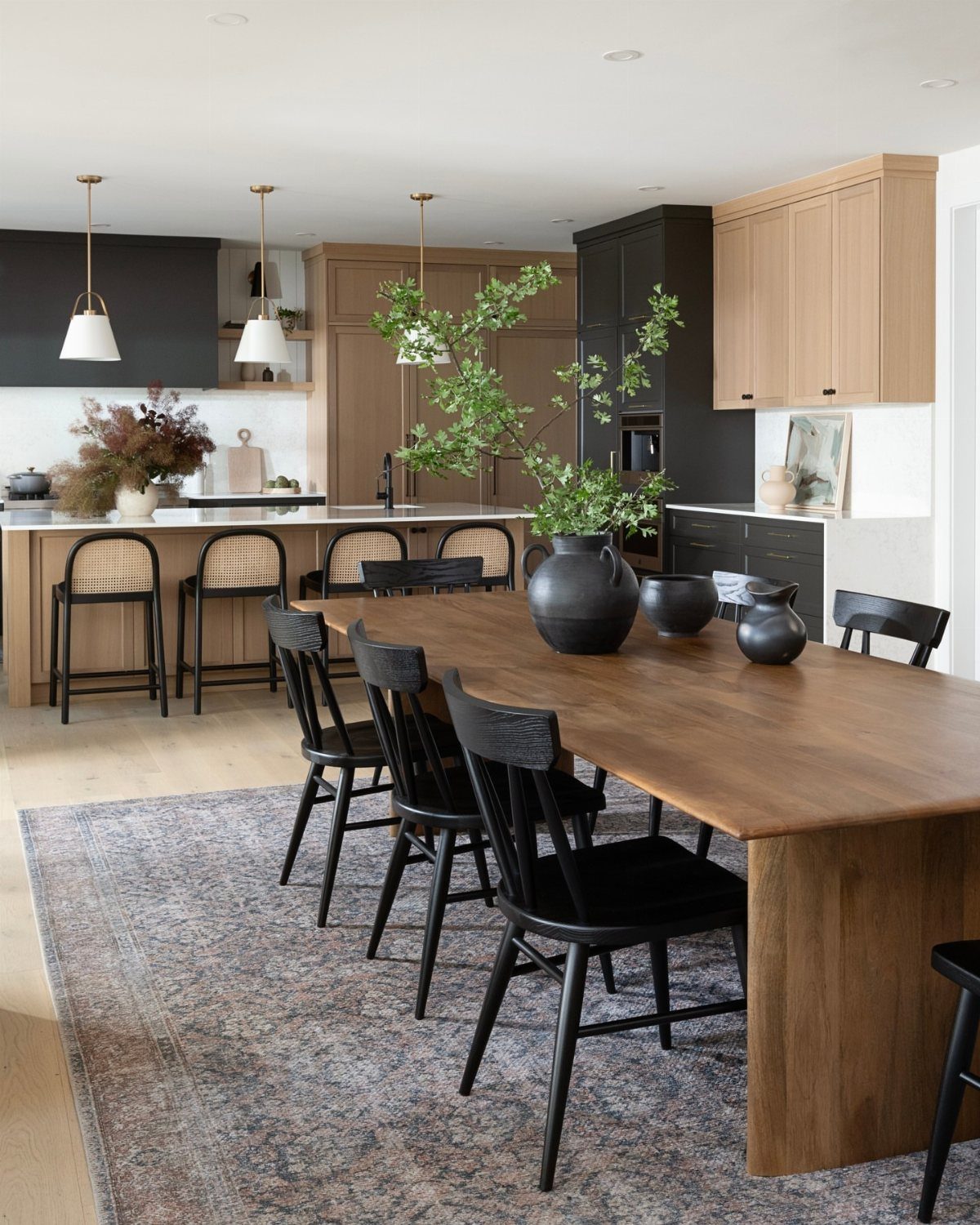 Wooden dining table with black chairs in an open concept kitchen and dining area.