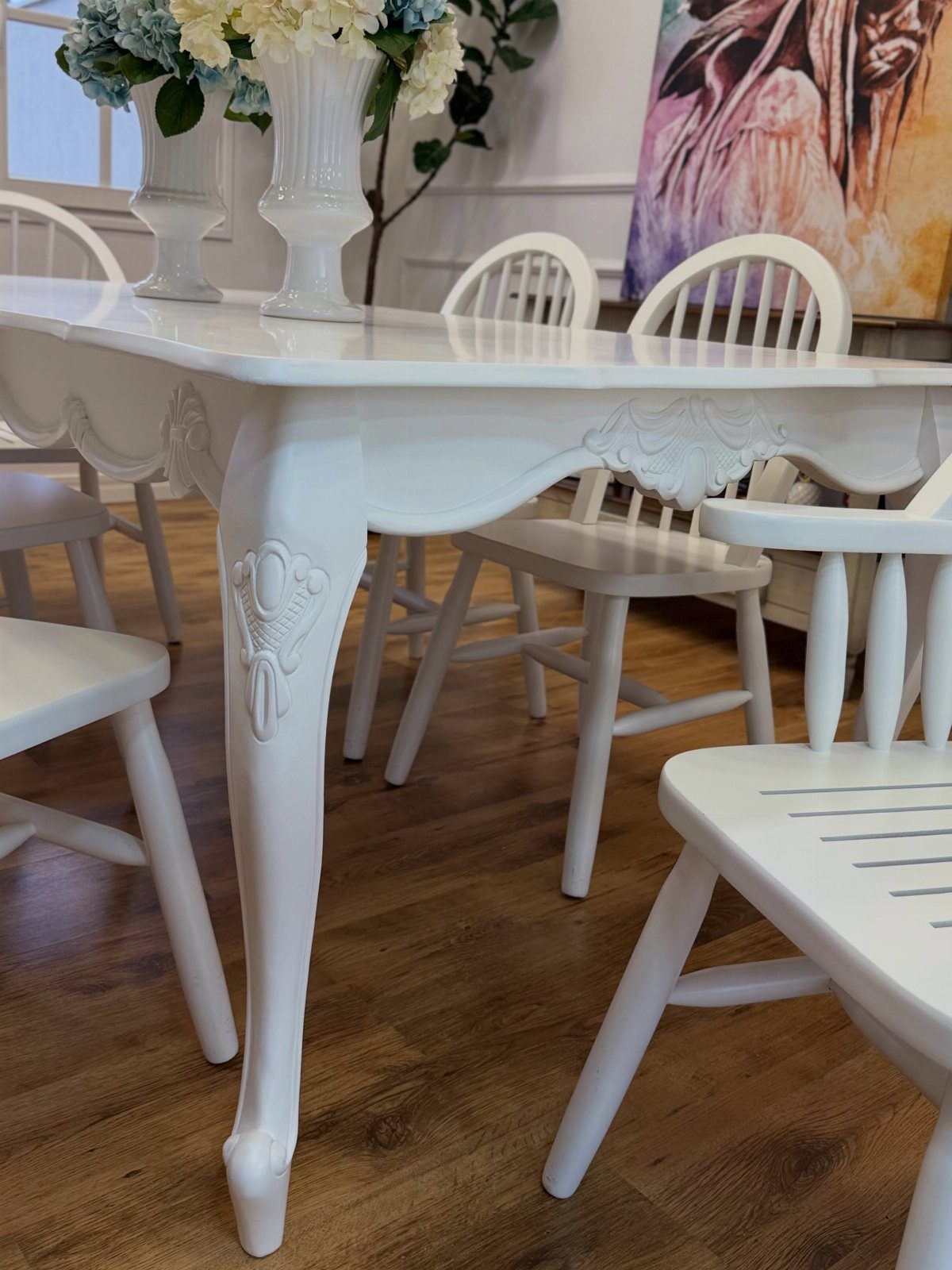 White painted wooden dining table with ornate carvings and matching white chairs.