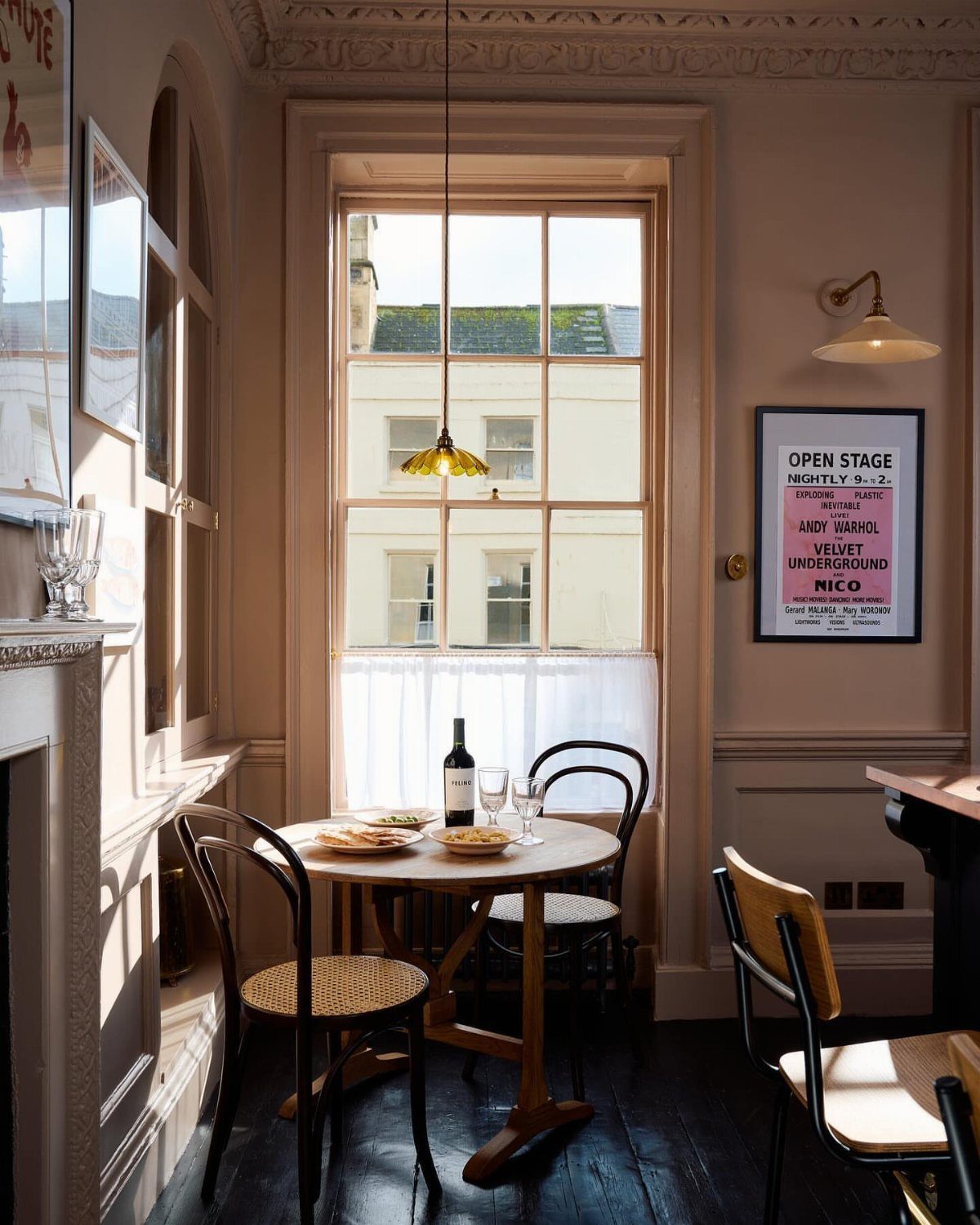 Round wooden table with chairs in a small, sunlit breakfast room with beige walls.