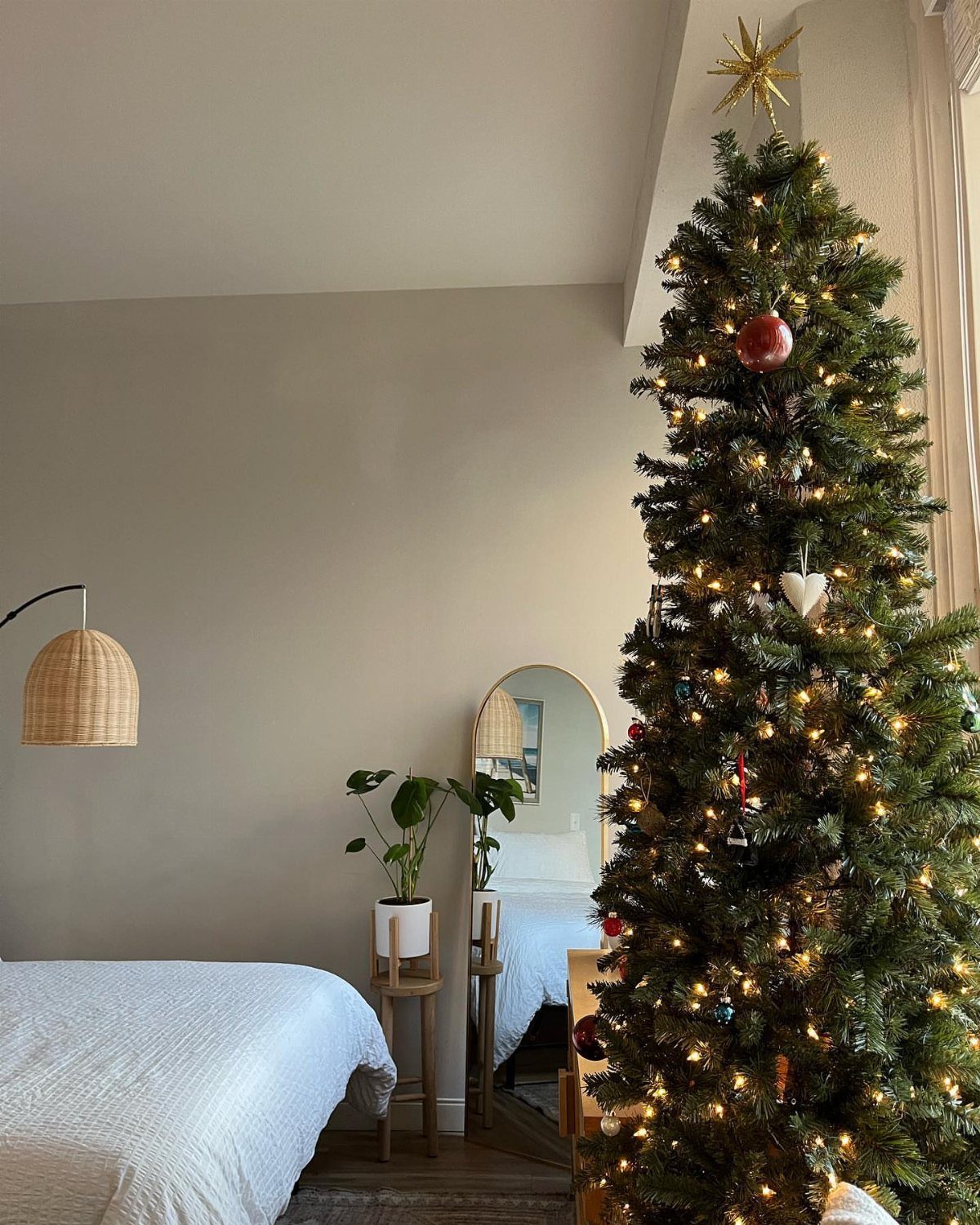 Decorated Christmas tree with warm lights in a small studio apartment bedroom setting.