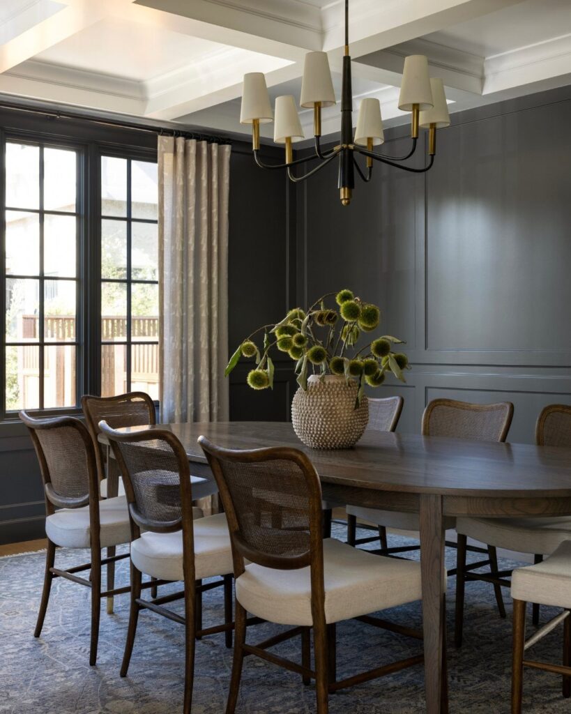 Dining room with grey paneled walls, wooden table, and cane-back chairs.