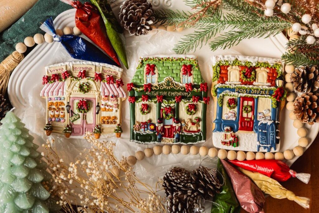 Iced cookies shaped like Victorian shops surrounded by pinecones and evergreen branches.