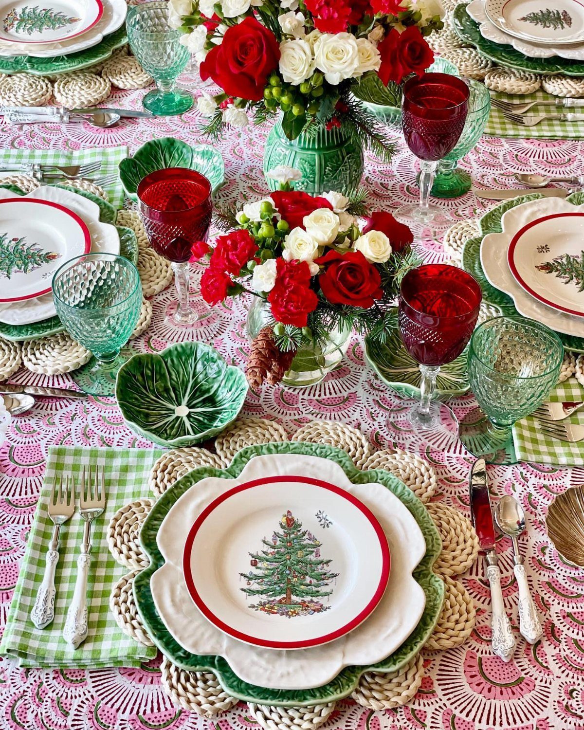 Vintage Christmas dishware and glassware set on a pink patterned tablecloth with red roses.